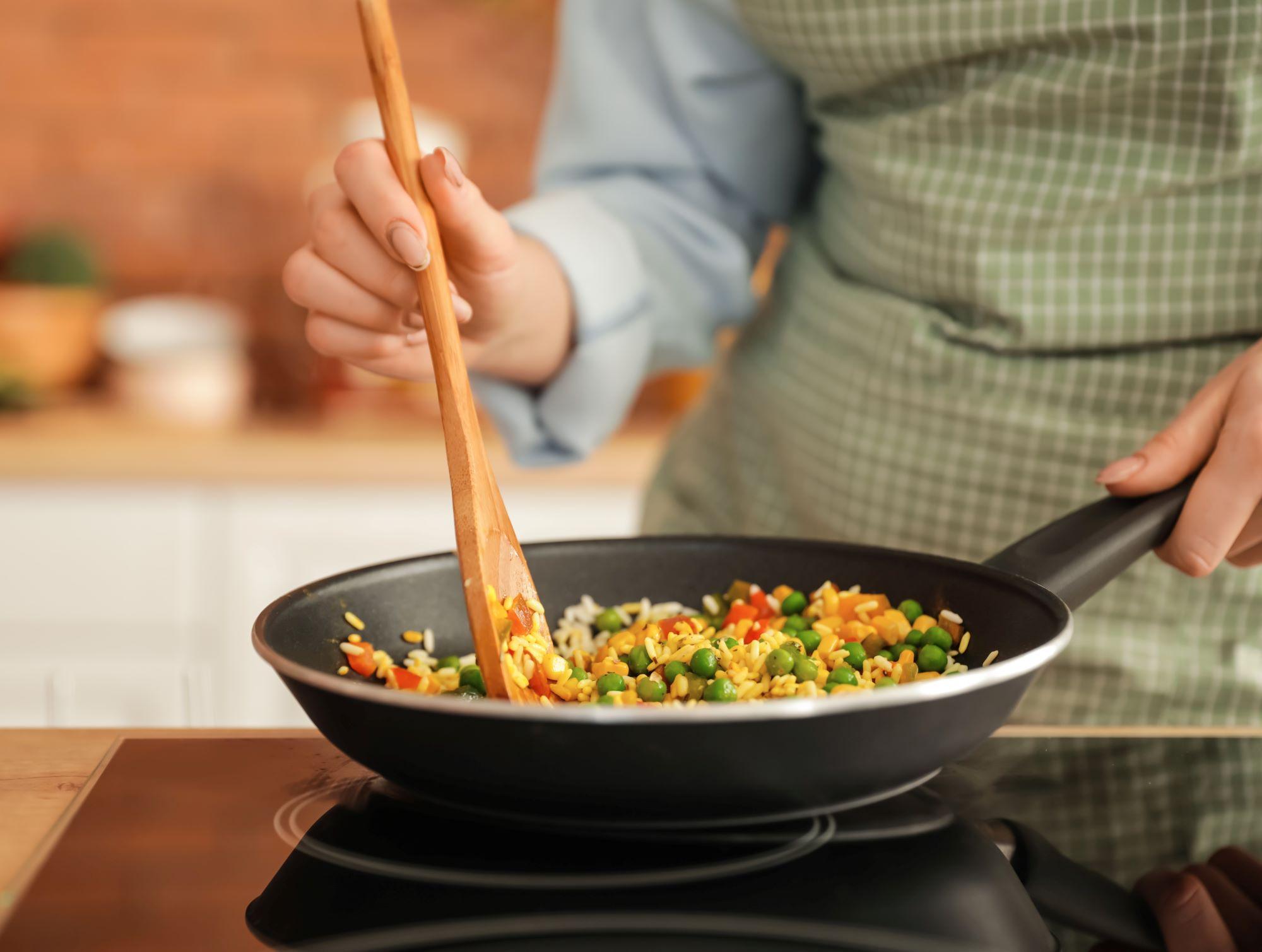 A young woman preparing a meal of rice, carrots, and peas on a stovetop.