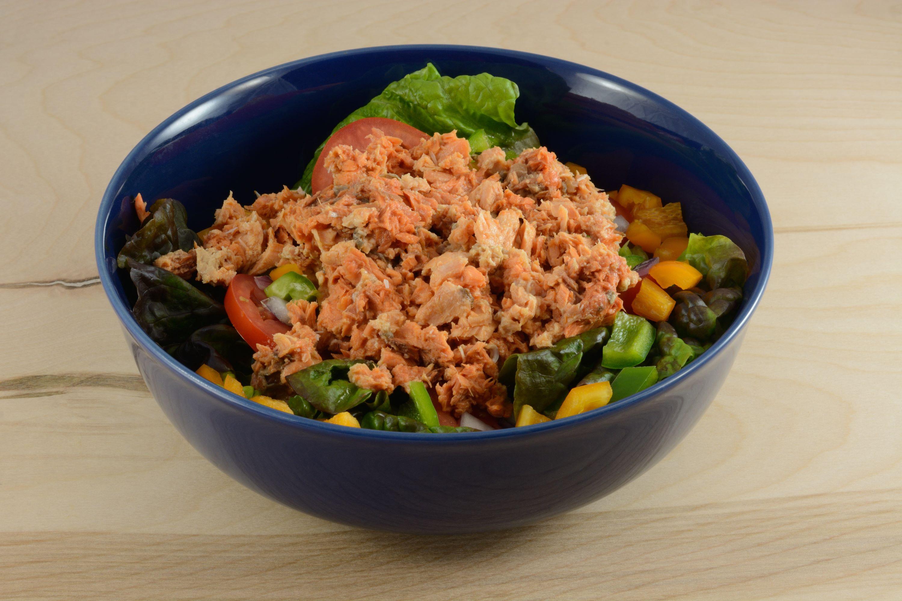 A blue bowl with a salad topped with canned salmon. 