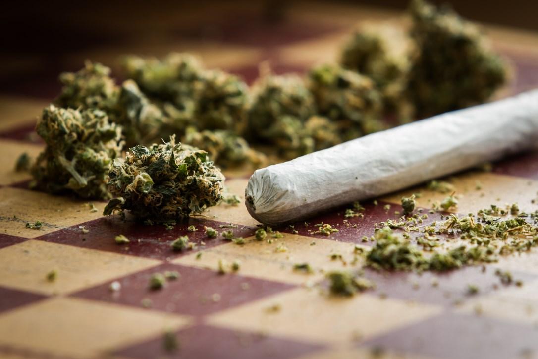 Closeup of marijuana joint and buds on a checkerboard table with a shallow depth of field.