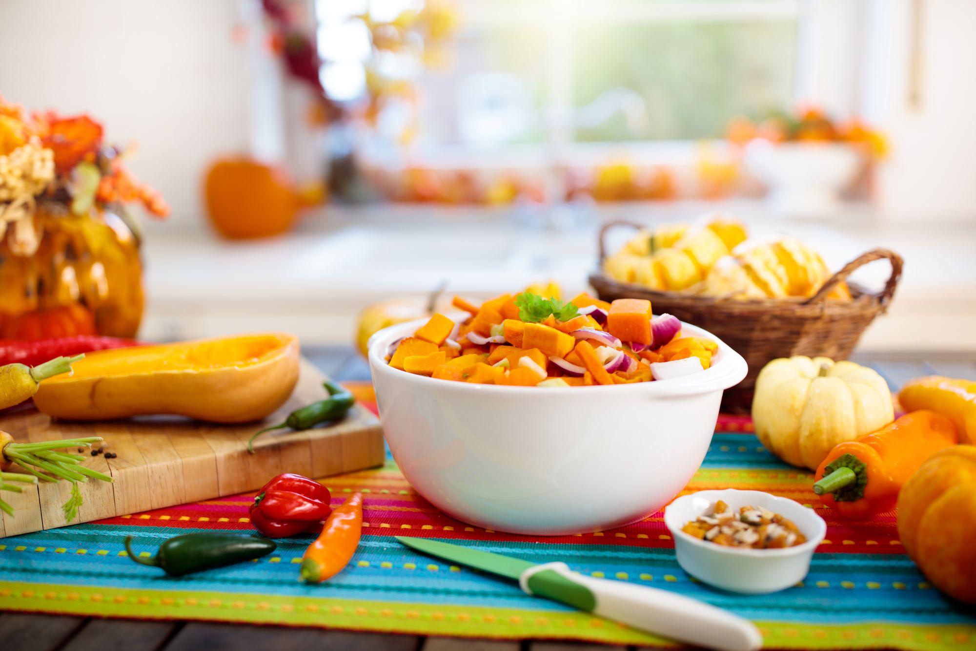A fall recipe with butternut squash, onions, and peppers in a white bowl. Surrounded by fall decor.