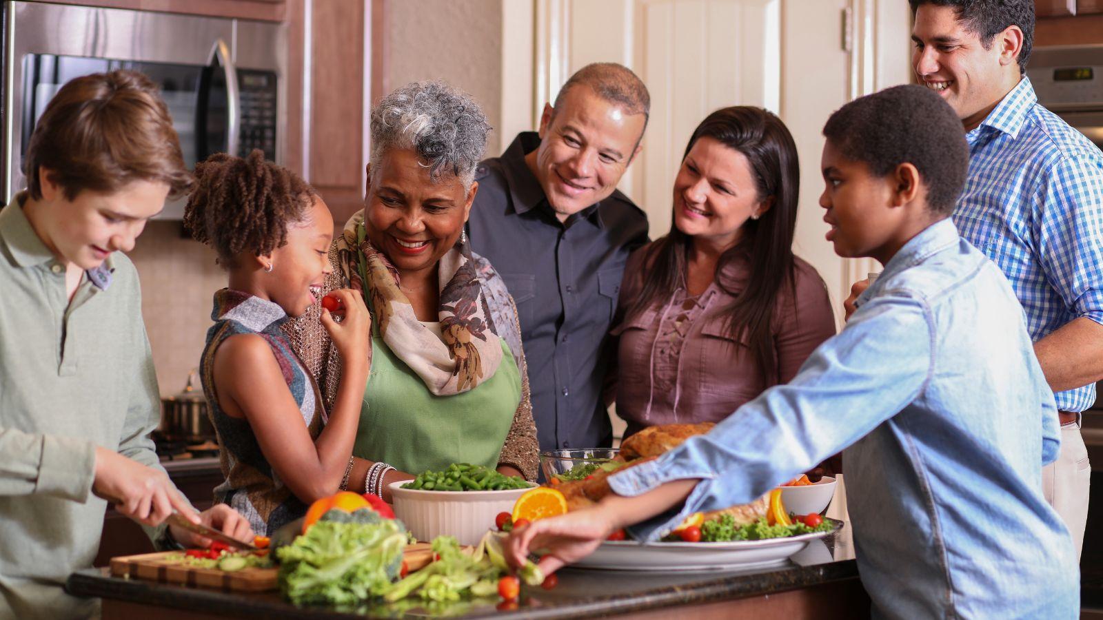 A multicultural family standing around an island sampling prepared foods. 