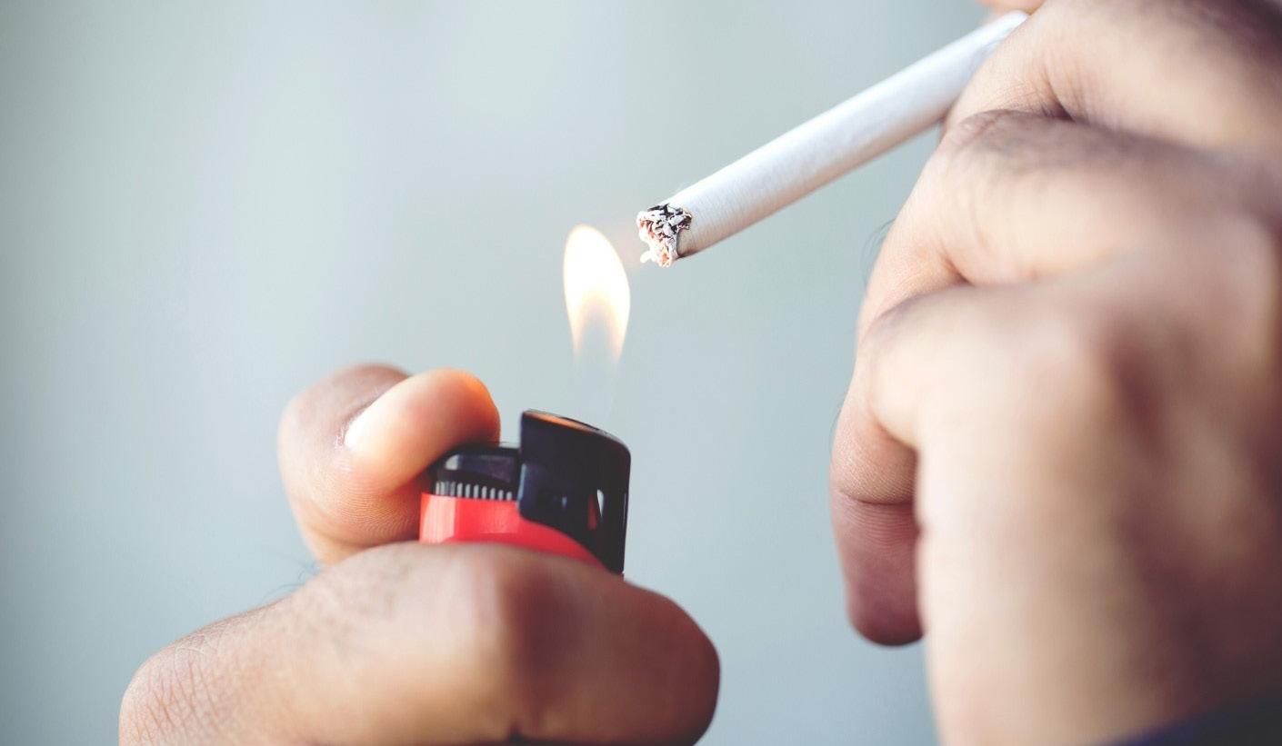  The scene depicts an individual holding a cigarette and igniting it with a bright red lighter, as the tip of the cigarette glows.