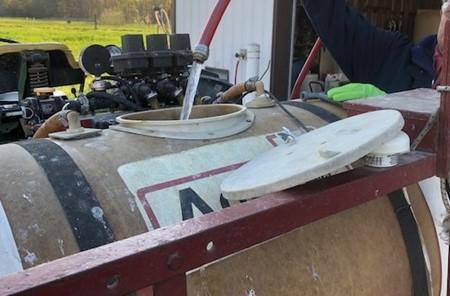 A large industrial holding tank is being filled with water from a hose.