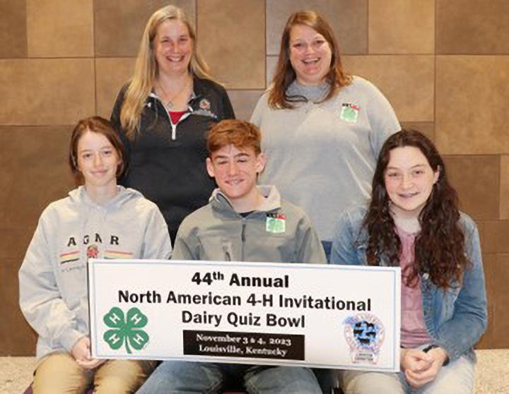 A group of five people poses with a sign for the "44th Annual North American 4-H Invitational Dairy Quiz Bowl." They smile in front of a brown tiled wall.