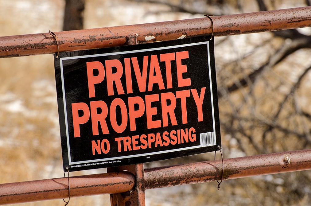 A black sign with "Private Property, No Trespassing" in bold red letters is attached to a rusted metal gate.