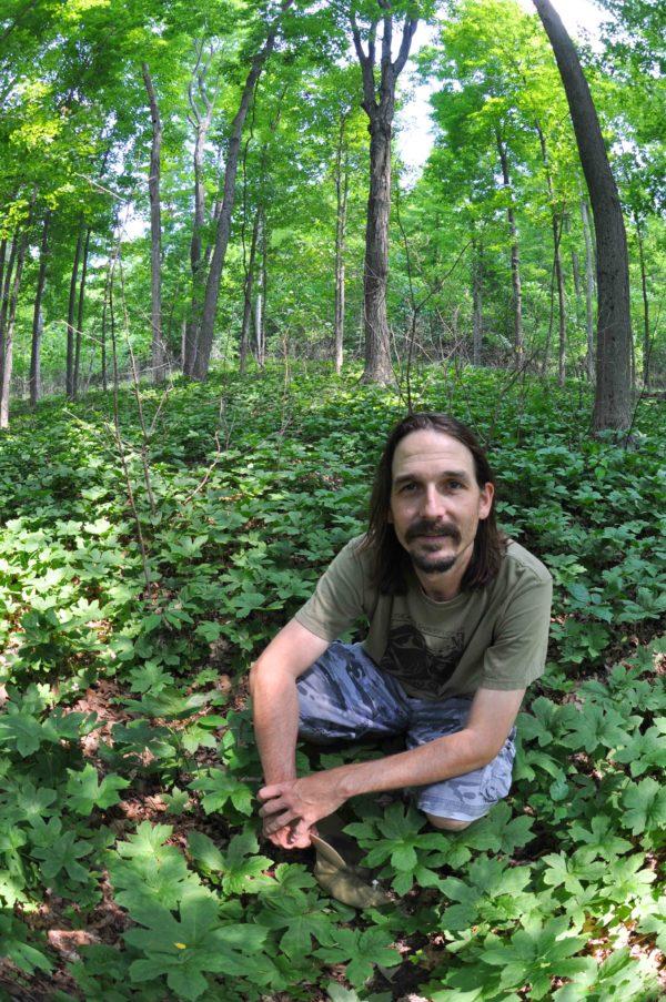 Dr. Eric Burkhart kneeling in the understory of a forest
