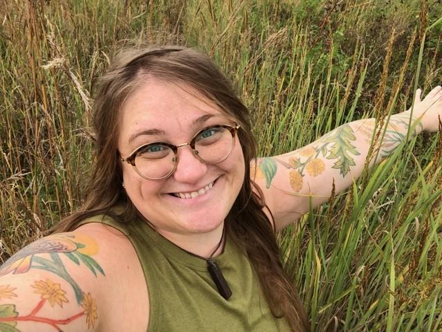 Dr. Liz Anna Kozik with outstretched arms in a meadow