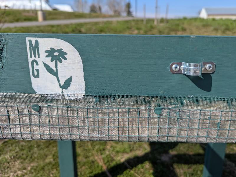 Close-up view of a Salad Table frame with an optional pipe bracket and two wide-headed nails anchoring the wire mesh wrapped over the frame's underside.