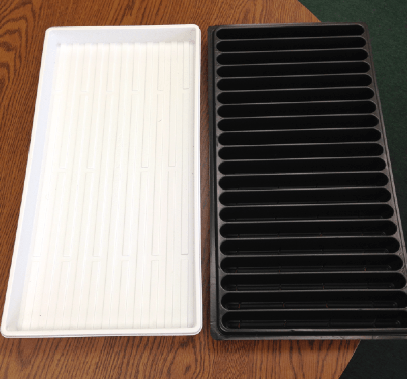 A set of two microgreens trays. One has narrow channels that span its width which will hold potting mix and the seeds. It is inserted into the other shallow, undrained tray.