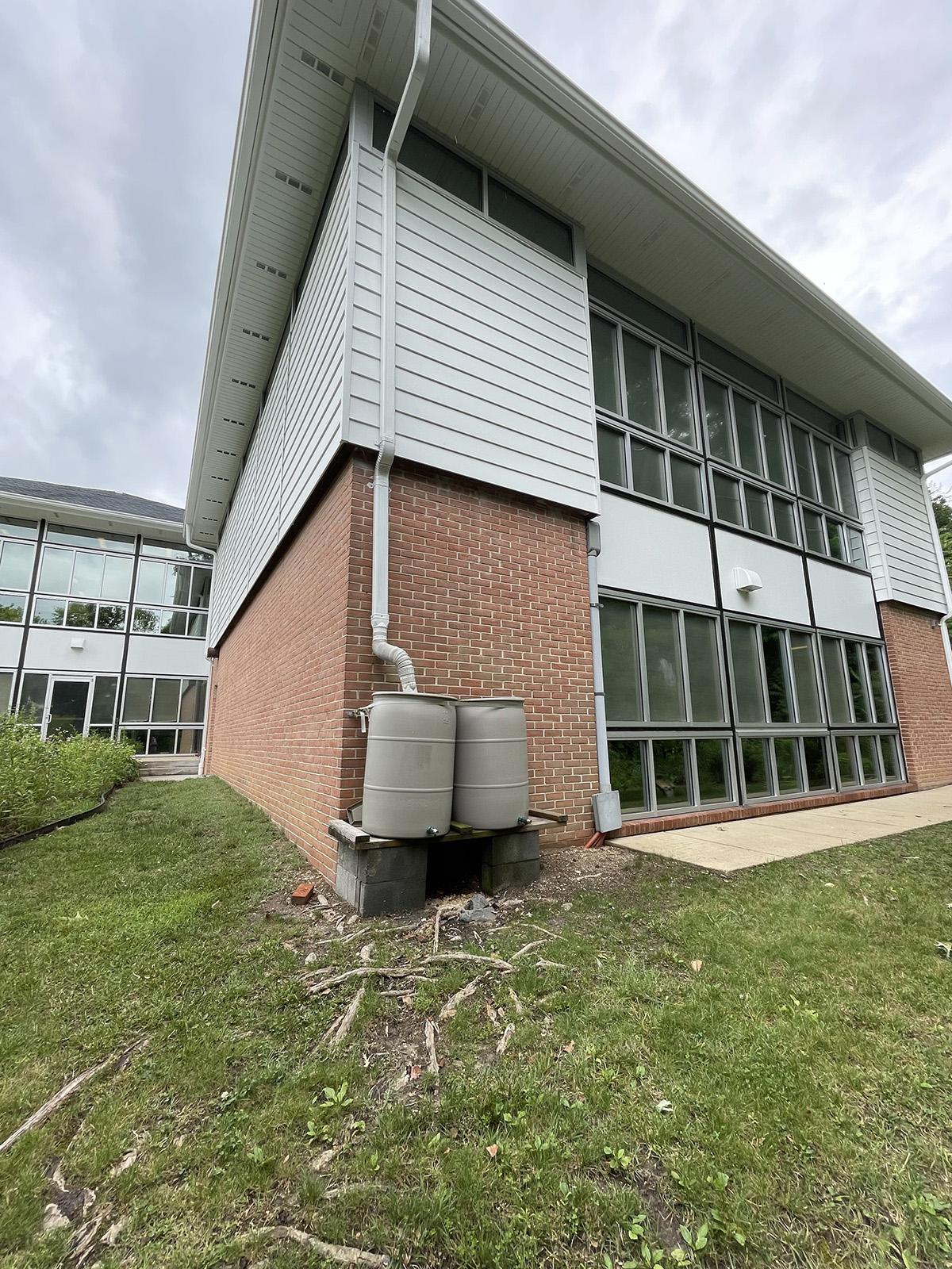 A large building with a downspout that is feeding rooftop runoff into two 55-gallon barrels.