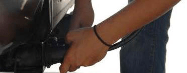Person’s hands connecting an electric cord to a bumper‑mounted input on the back of a vehicle.