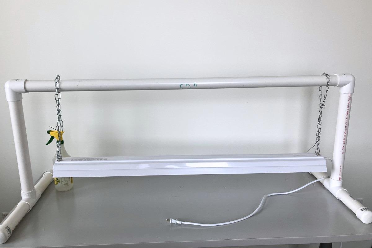 Sections of plastic 1.5-inch diameter pipe assembled into a footed stand 4 feet long. A light fixture about 3 feet long is suspended by adjustable chains from the top bar.