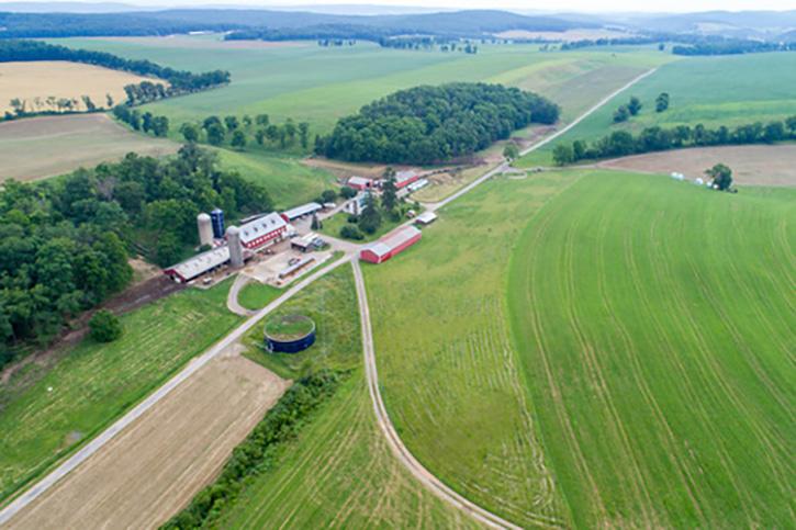 Aerial view of farm, showing farm fields with row crops, forested areas, farm buildings, manure structures, and silos.