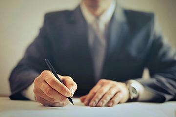 A man wearing a suit and tie is writing on a piece of paper.