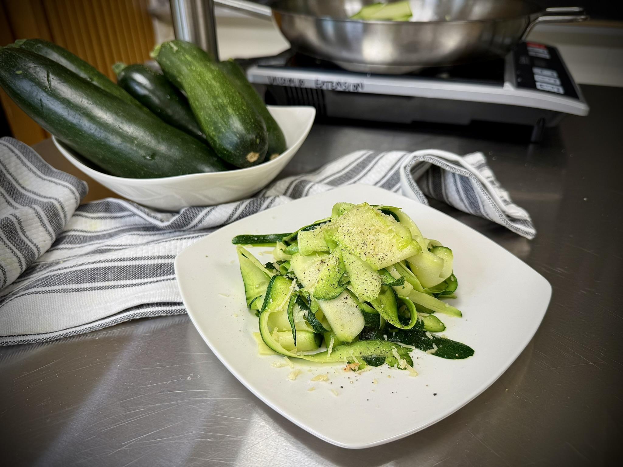 Shaved zucchini or zoodles on a plate, set in front of a bowl of fresh zucchini