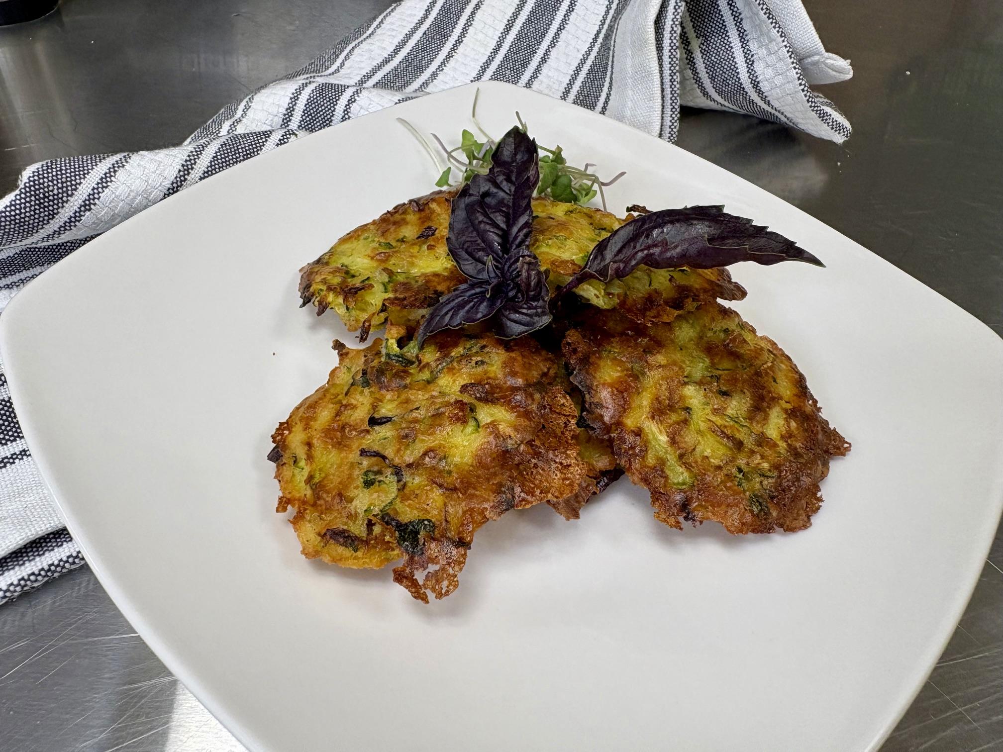 Grated zucchini patties stacked on a plate with basil in the middle