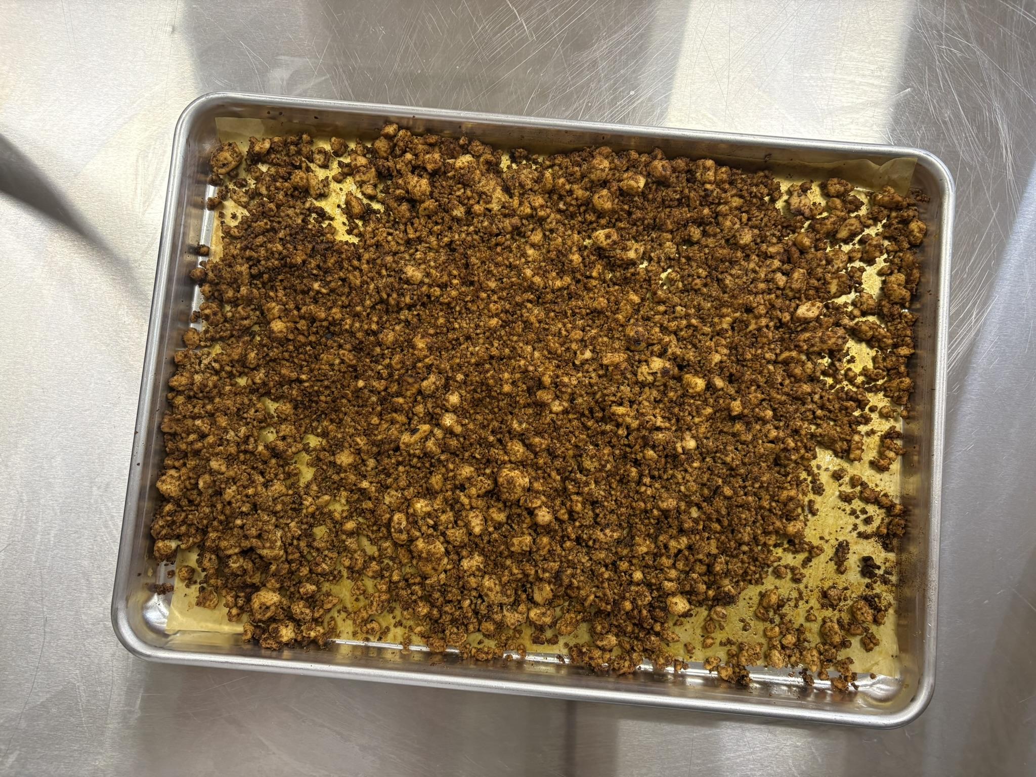 Cooked Tofu Crumbles spread across a metal sheet pan on a metal surface