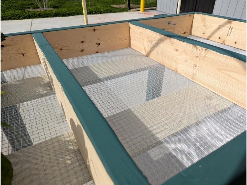 Close-up of the center section of a Salad Table. Two wide support boards spanning the length of the table are visible through the mesh on the bottom of the table.