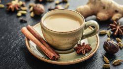 mug of chai sitting on a saucer with a cinnamon stick and star anise on the plate surrounded by other spices