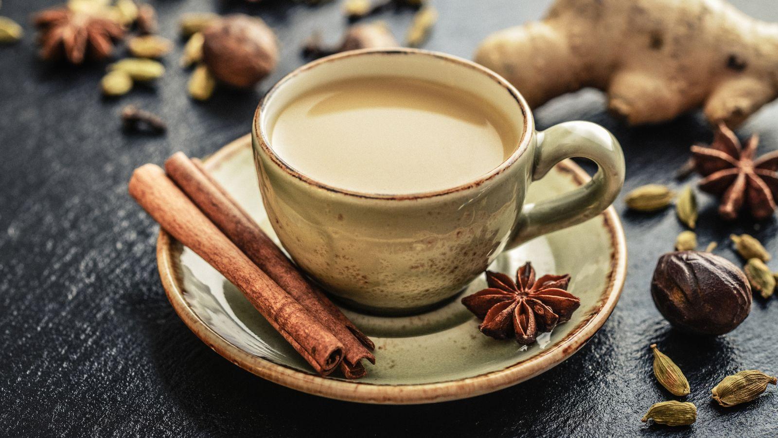 mug of chai sitting on a saucer with a cinnamon stick and star anise on the plate surrounded by other spices