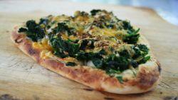 cheese and cooked spinach on top of a piece of toasted naan, sitting on a wooden counter