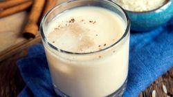glass of horchata with ice on a blue napkin sitting on a table by cinnamon sticks