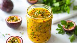 passion fruit vinaigrette in a glass jar sitting on a white table surrounded by fresh passion fruit