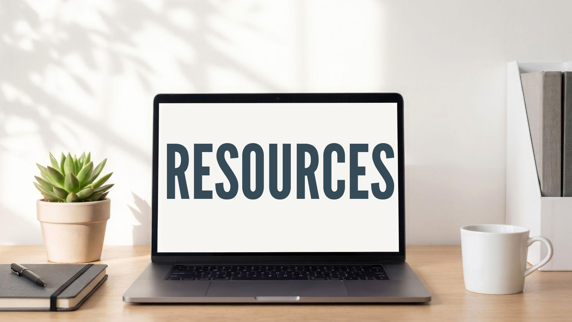 Resources banner on a laptop screen, sitting on a desk next to a plant, notebook and coffee mug