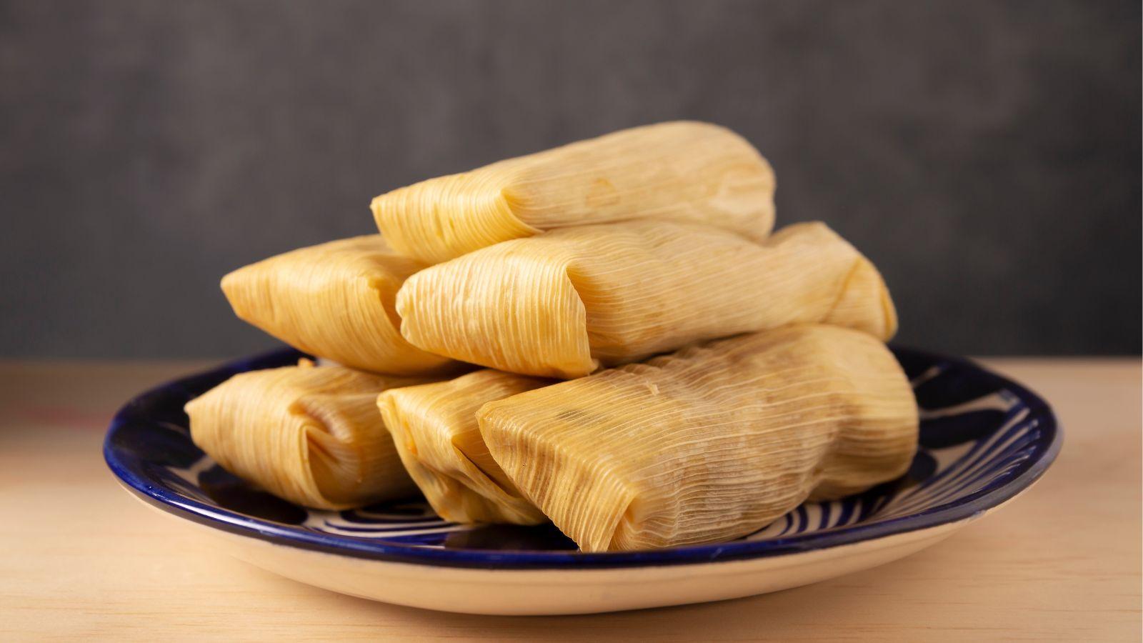 stacked tamales sitting on a dark plate on top of a wooden table with a gray background